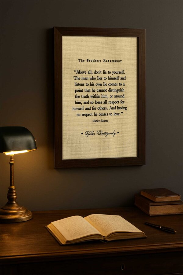 Framed quote from The Brothers Karamazov hangs on a dark wall above a vintage wood desk with an open book, a fountain pen, and a warm brass lamp casting soft light.