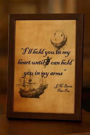 Wood-framed "I'll hold you in my heart" quote print photographed on a wooden table in warm light, with textured parchment background and pirate ship illustration.