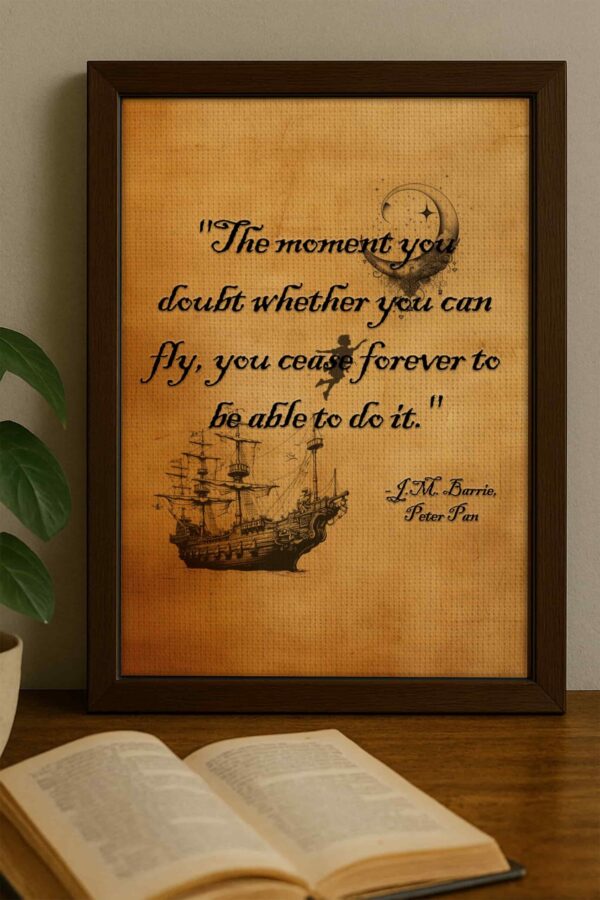 Close-up of framed Peter Pan quote leaning on a wooden surface with an open book in the foreground and leafy plant to the side.