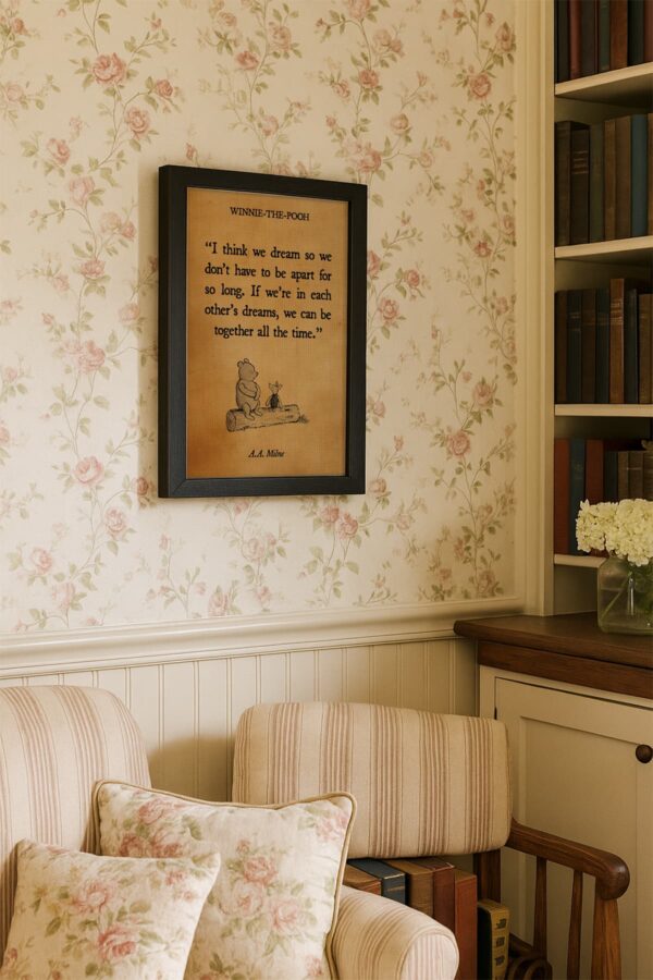 Winnie-the-Pooh quote canvas with the line “If we’re in each other’s dreams, we can be together all the time,” displayed in a black frame on floral wallpaper above a floral-accented reading chair.