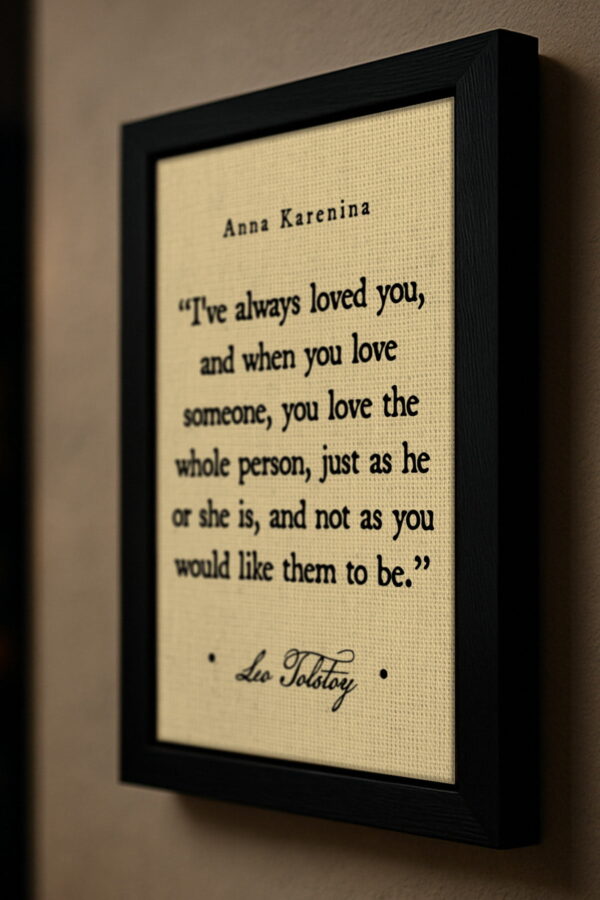 A close-up side view of the framed Tolstoy quote from Anna Karenina, mounted on a neutral wall. The black frame and canvas texture are visible in detail, highlighting the elegant typography.