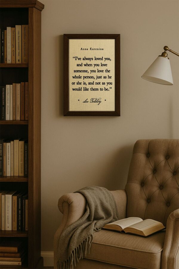 The framed quote hangs above a cozy reading chair and blanket in a minimalist room with warm beige tones and a wooden bookshelf. A soft reading light completes the calm, literary vibe.