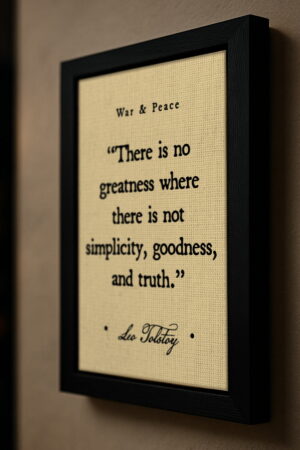 Side-angle view of a black-framed canvas featuring Tolstoy’s quote on a beige textured background, mounted on a modern neutral-toned wall.
