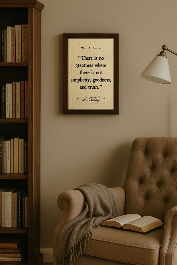 Cozy reading nook scene with a framed Tolstoy quote print hanging near a tufted chair, open book, and wooden bookshelf filled with classic literature.